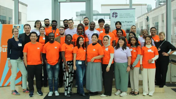 Gruppenfoto der Stipendiat*innen und Organisator*innen im Haus des Evangelischen Werkes für Diakonie und Entwicklung in Berlin, wo auch Brot für die Welt den Sitz hat. Die Teilnehmenden des DNK/LWB tragen violette T-Shirts, die von Brot für die Welt orangefarbene. Foto: DNK/LWB Helene Maria Guib